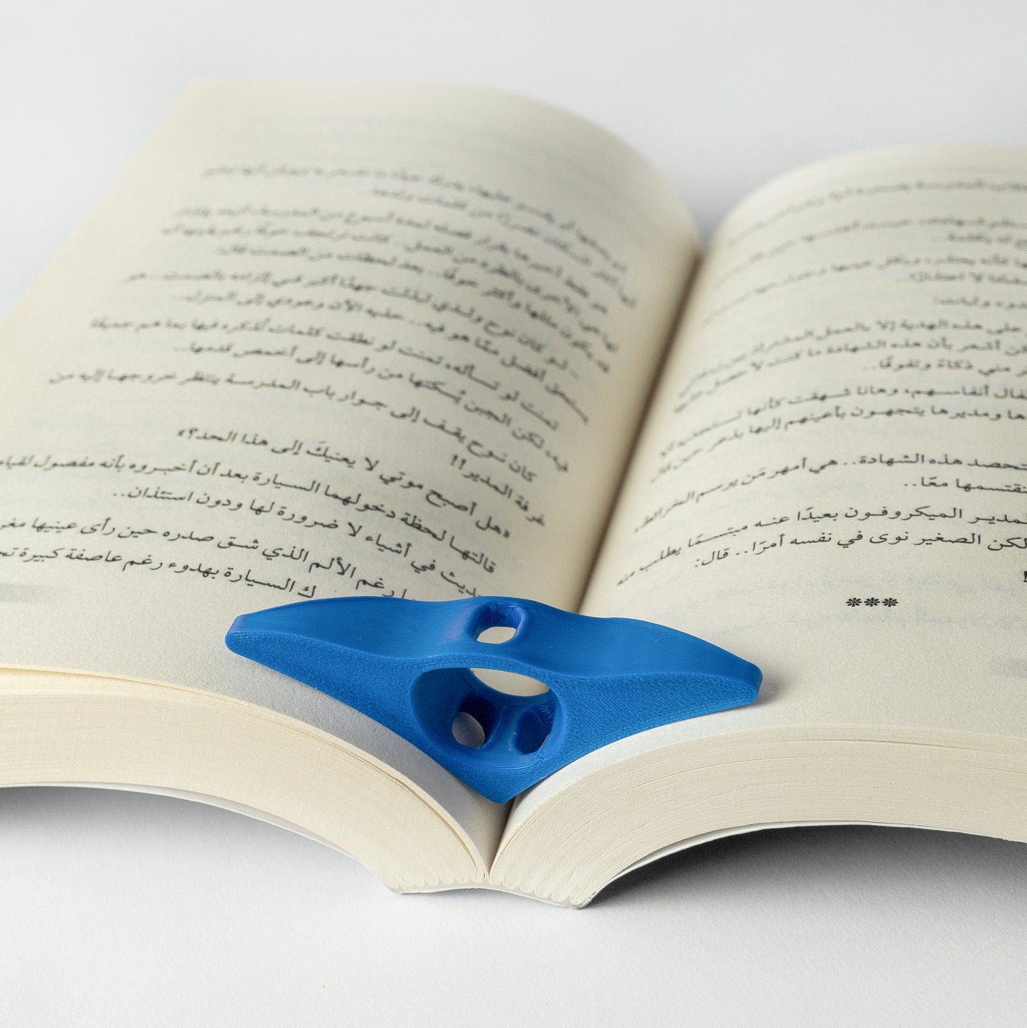 A blue thumb book holder placed on an open book, demonstrating its use in keeping the pages open.