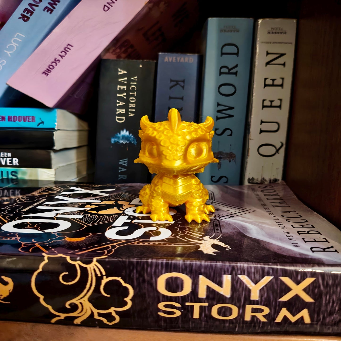 Gold figurine on a book titled 'Onyx Storm' with other books in the background