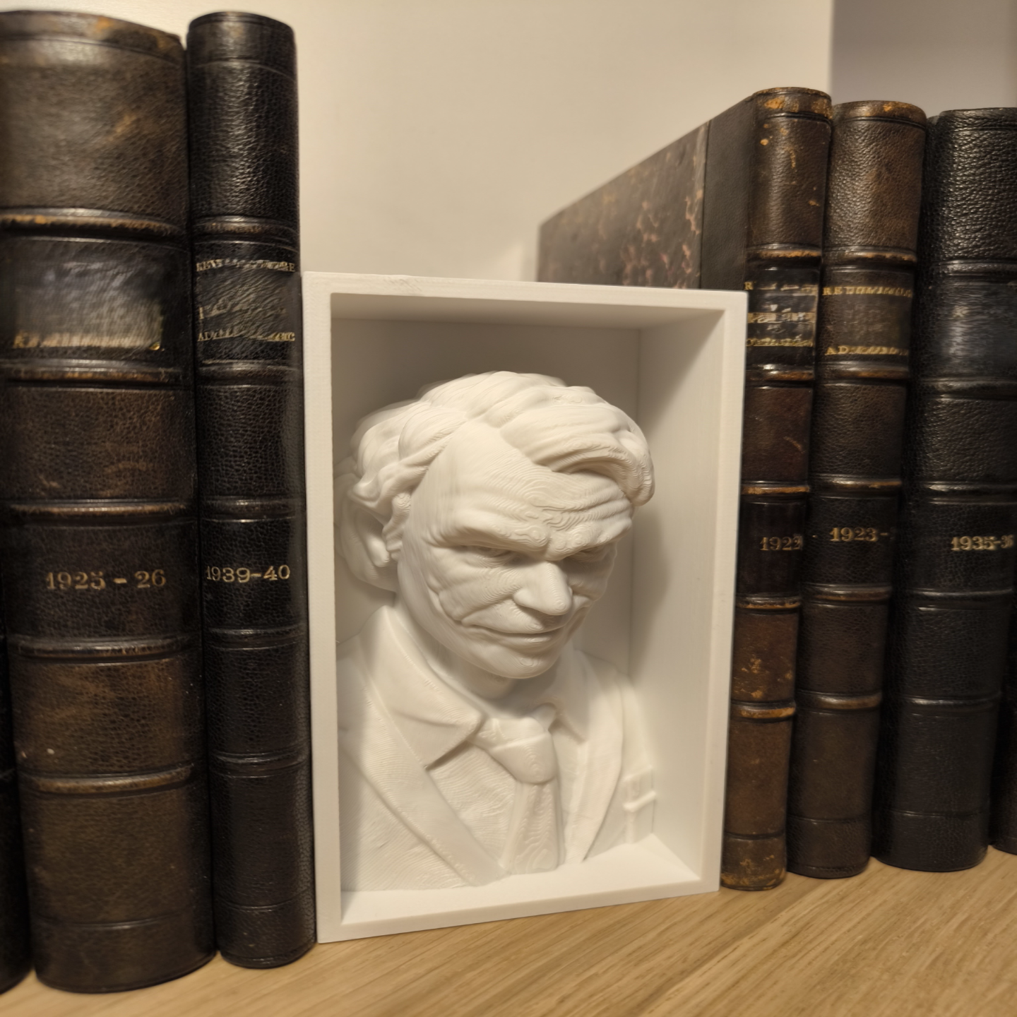 White bust sculpture of a man surrounded by old leather-bound books on a wooden surface.