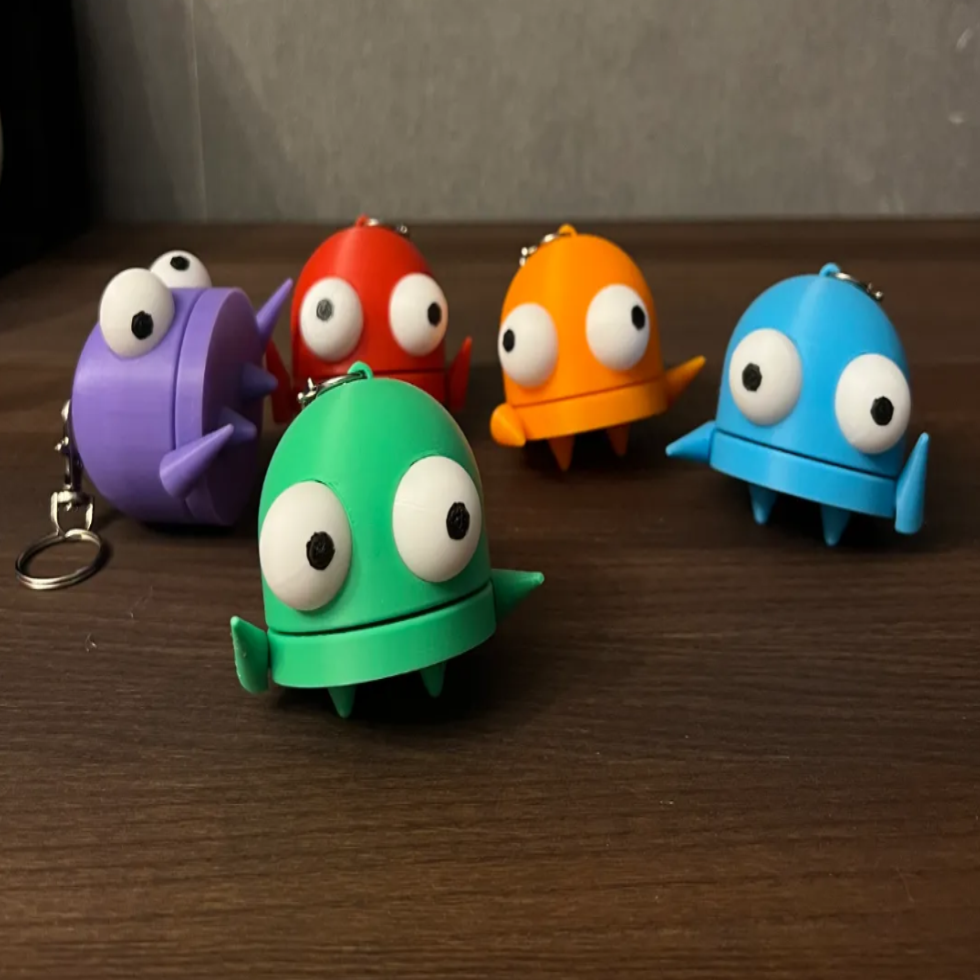 A collection of colorful toy keychains designed to look like robots in various colors, including green, purple, red, orange, and blue.