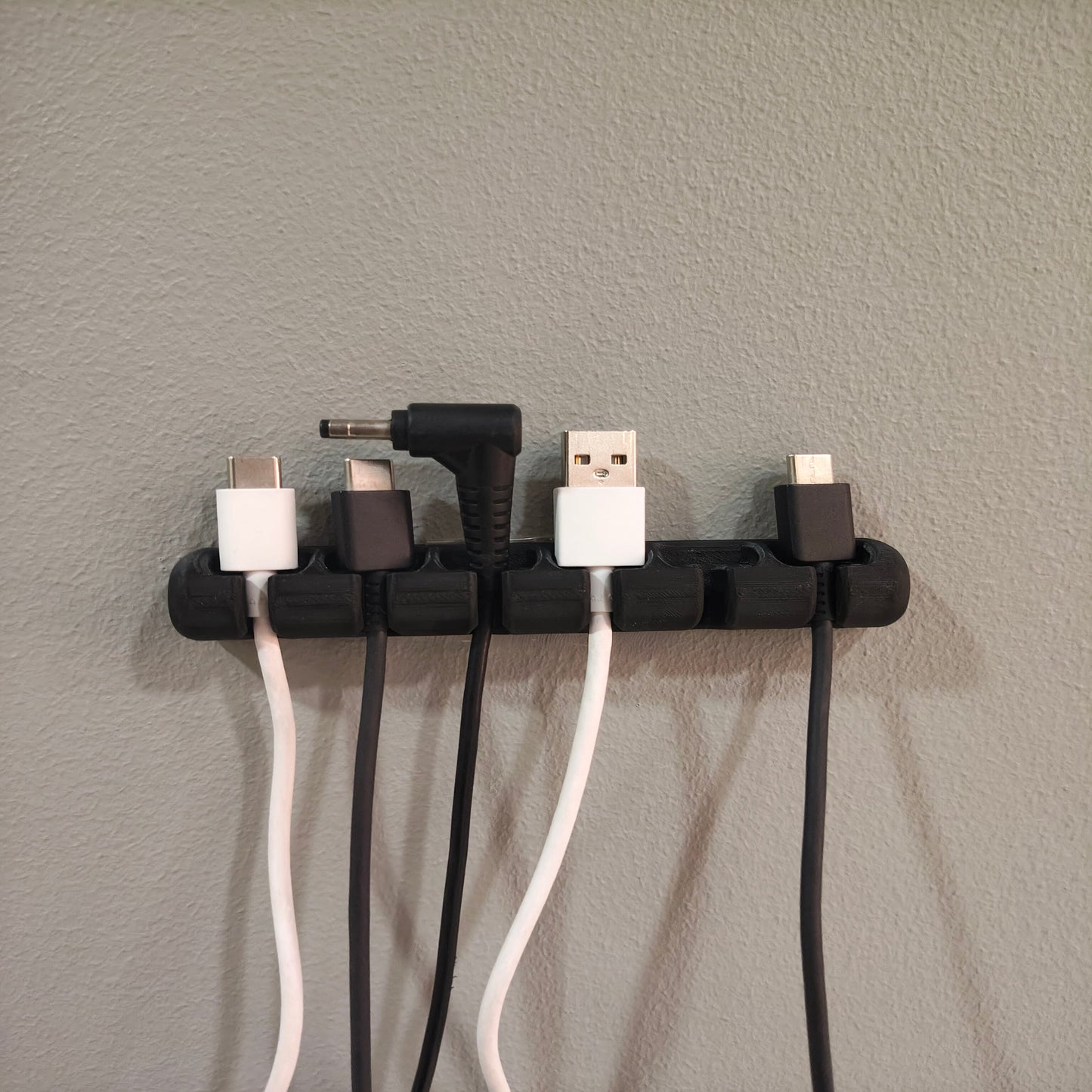 Wall-mounted cable organizer holding various electronic plugs against a gray wall.