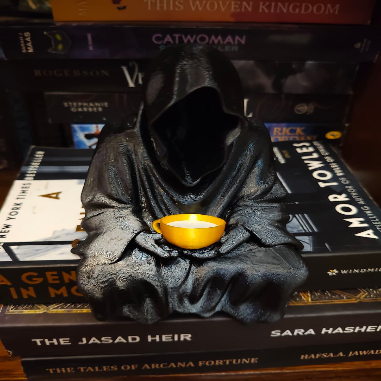 Statue of a hooded figure holding a yellow cup on top of books