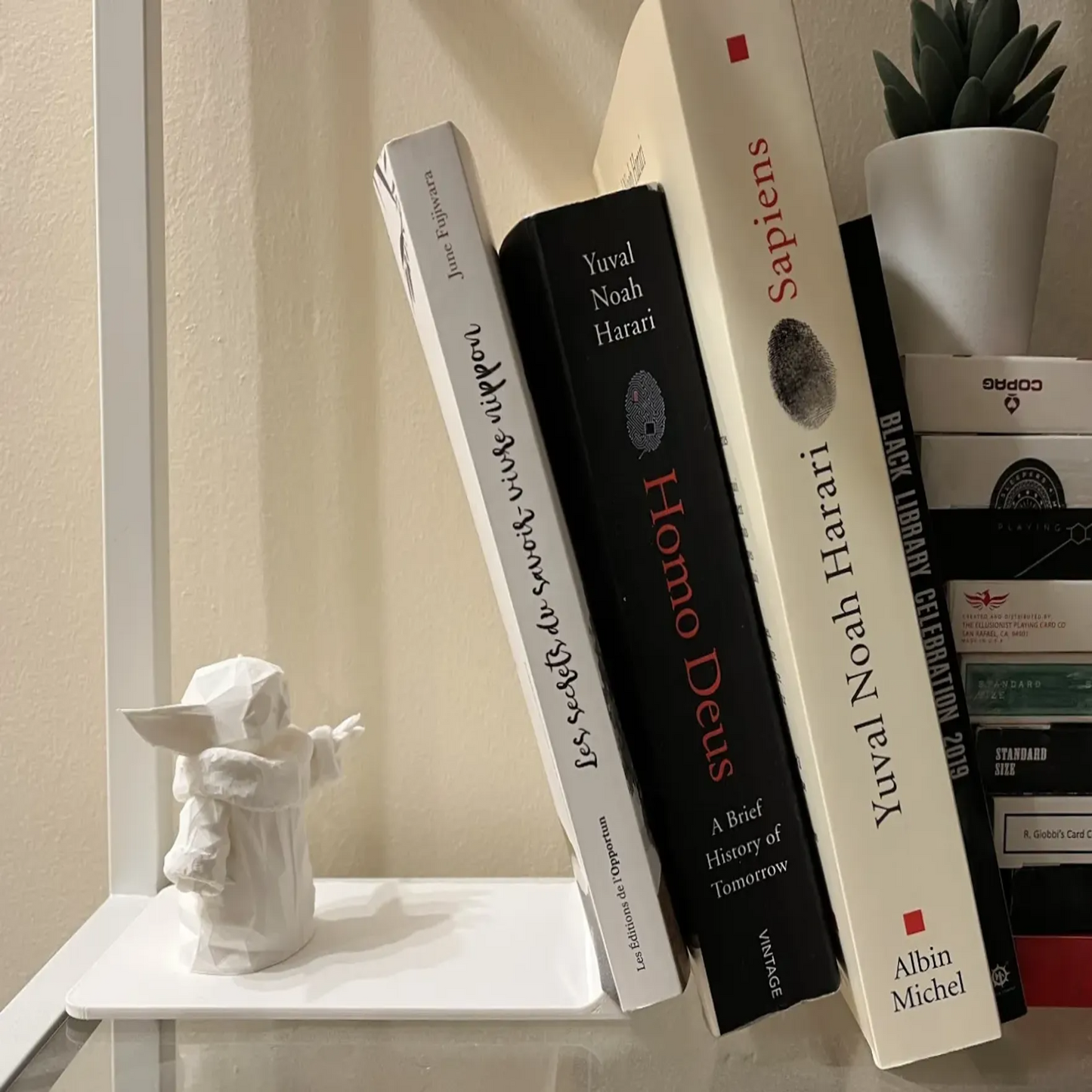 Stack of books on a shelf with a small statue and plant