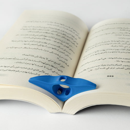 A blue thumb book holder placed on an open book, demonstrating its use in keeping the pages open.