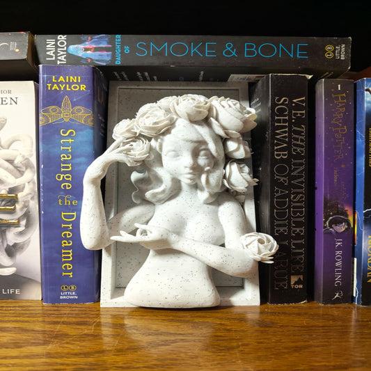 White sculpture of a woman with flowers among books on a wooden surface